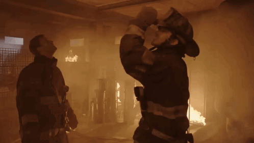 Fireman Holding Hose In Front Of Burning Building GIF