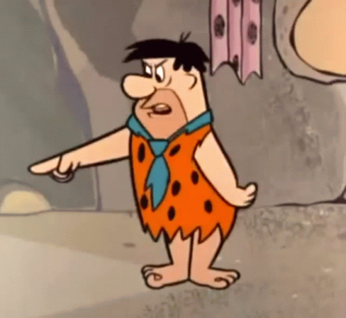 Flintstone From The Flintstones Is Standing In Front Of A Rock Wall And Pointing At Something . GIF