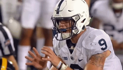 Football Player in White Helmet 9 Jersey Sitting on Field With Hands Outstretched