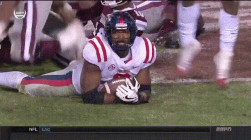 Football Player Lying on Field Holding Ball with NC Helmet