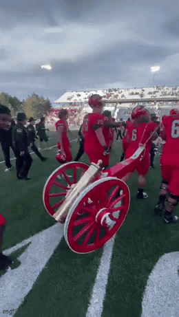Football Players Holding Cannon on Field