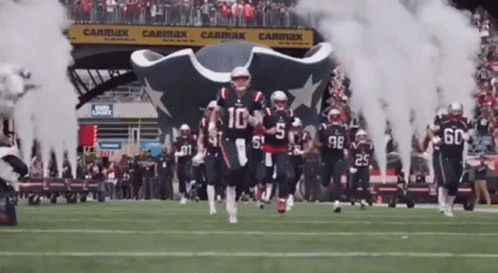 Football Players Running on Field With Smoke From Tunnel