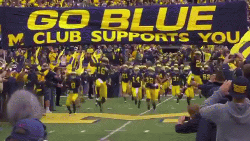 Football Team Running With Go Blue M Club Banner