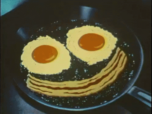 Fried Eggs And Bacon In A Frying Pan With A Smiley Face Drawn On It GIF