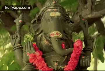 Ganesha Statue Sitting Under Tree With Red Flower Garland