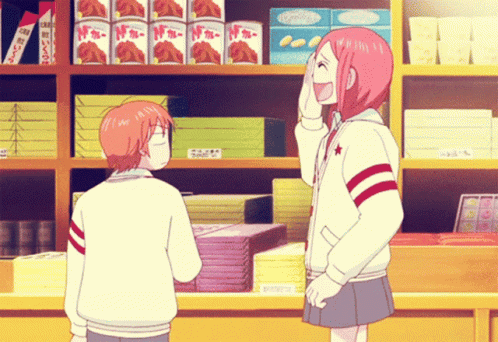 Girl With Pink Hair Laughing Next to Boy in Front of Shelf With Boxes