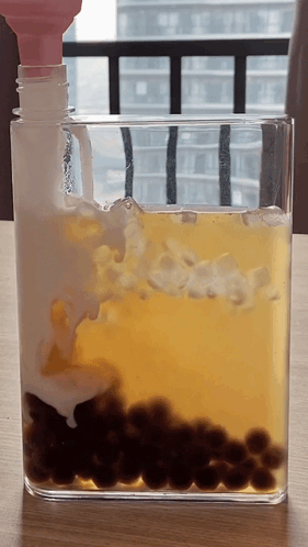 Glass Container With Yellow Liquid And Black Balls GIF