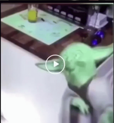 Green Alien Laying On Table With Play Button GIF