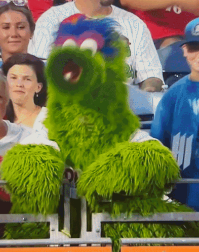 Green Monster Mascot Sitting In Stands At Sports Game GIF