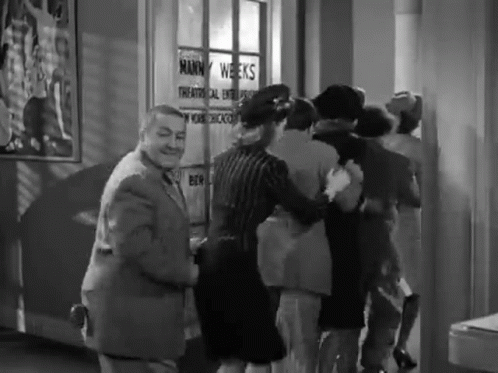 Group Of People In Front Of Mann Weeks Sign GIF