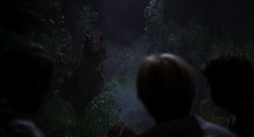Group Of People Looking At Dinosaur In Dark Forest GIF