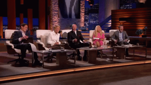 Group Of People Sitting At Tables On Stage GIF