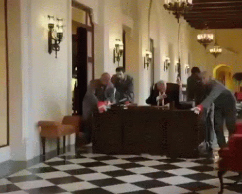 Group of People Standing Around Table in Hallway With Checkered Floor