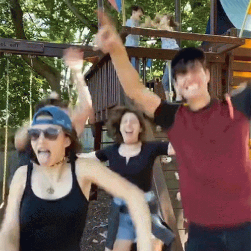 Group Of People With Arms Up In Front Of Playground GIF