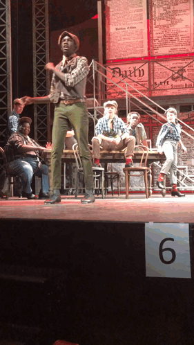 Group on Stage With 6 Sign