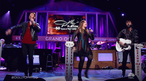 Group Singing and Playing Guitars Behind Dolly Parton Screen