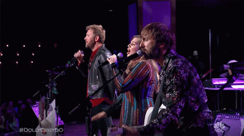 Group Singing Into Microphones on Stage With NBC Logo