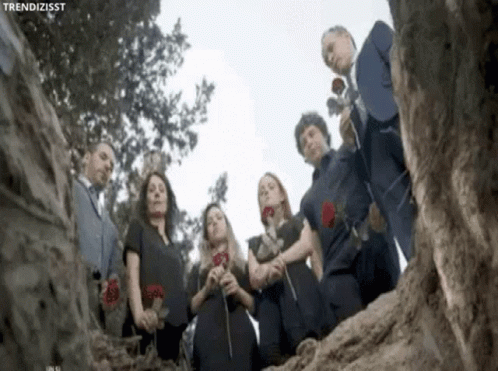 Group Standing In Circle Holding Roses In Front Of Tree GIF