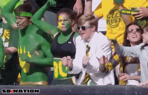 Group With Green and Yellow Paint Cheering in Stadium Saying Senation