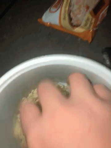 Hand Reaching Into Bowl of Noodles