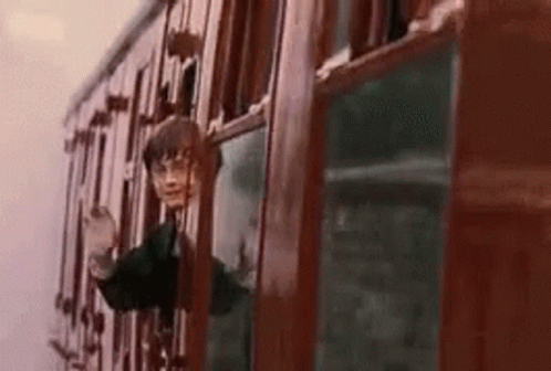 harry potter is looking out of a train window while riding a train .