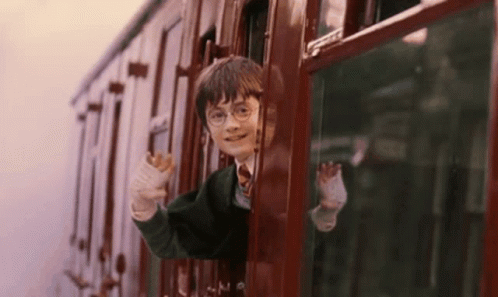 harry potter is riding a train and waving out of the window .