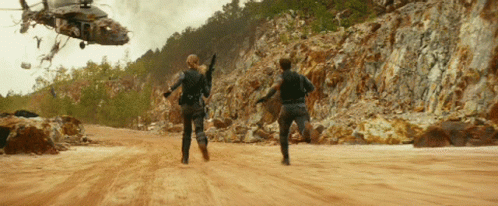 Helicopter Flying Over Dirt Road With Two People Running
