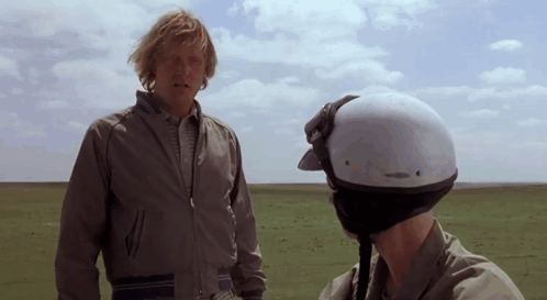 Helmeted Man Talking To Man In Field GIF