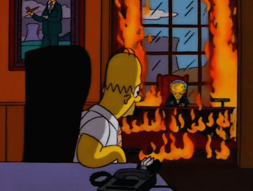 Homer Simpson Is Sitting At A Desk In Front Of A Burning Window GIF