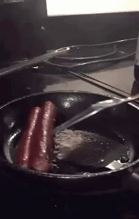 Hot Dogs Are Being Cooked In A Frying Pan With A Spatula GIF