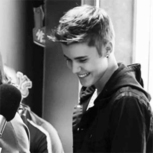 Justin Bieber Is Smiling In A Black And White Photo While Standing In Front Of A Microphone . GIF