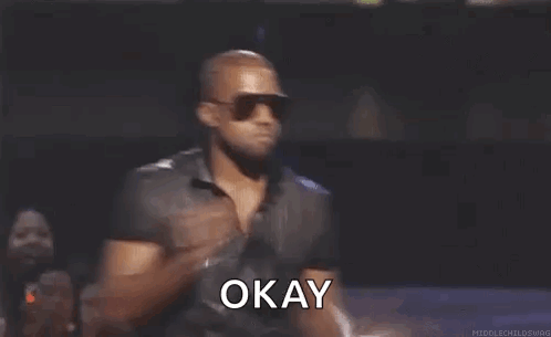 Kanye West in Sunglasses and Black Shirt Holding Microphone Saying Okay