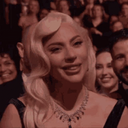 Lady Gaga Is Smiling While Sitting In A Crowd Of People . GIF