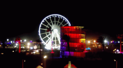 Large Ferris Wheel Lit Up At Night In Front Of Building GIF