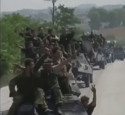 Large Group Sitting on Military Vehicles on Road