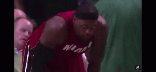 lebron james is wearing a headband and a miami jersey while sitting on the bench .