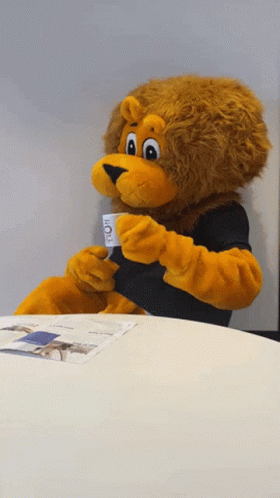 Lion Mascot Sitting at Table Holding Coffee Cup