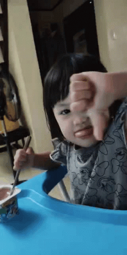 Little Girl Eating Yogurt With Spoon Giving Thumbs Down GIF