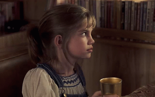 Little Girl Holding Cup in Front of Bookshelf