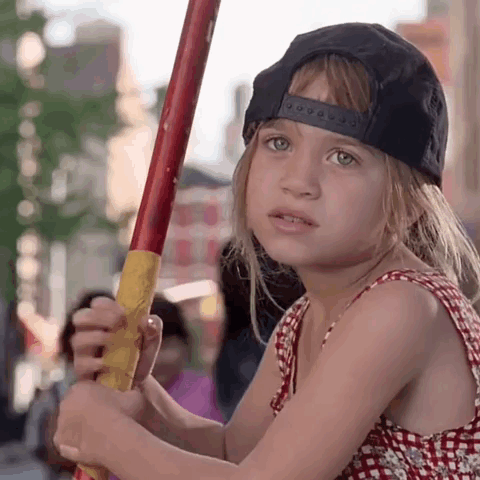 Little Girl in Black Hat Holding Red and Yellow Stick