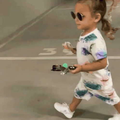 Little Girl in Sunglasses and Floral Outfit Walking in Parking Lot