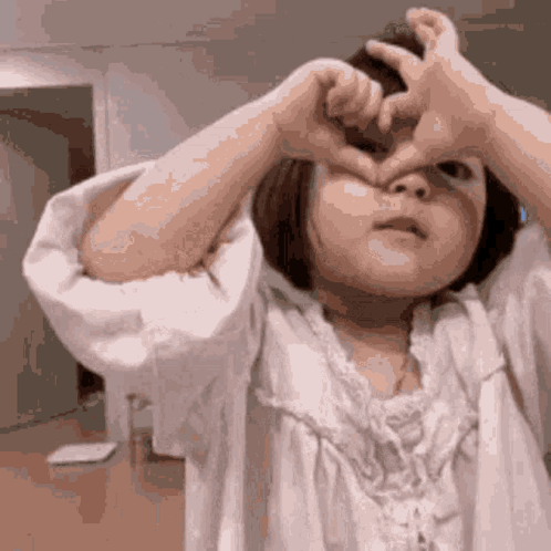 Little Girl Making Heart With Hands Over Eyes GIF