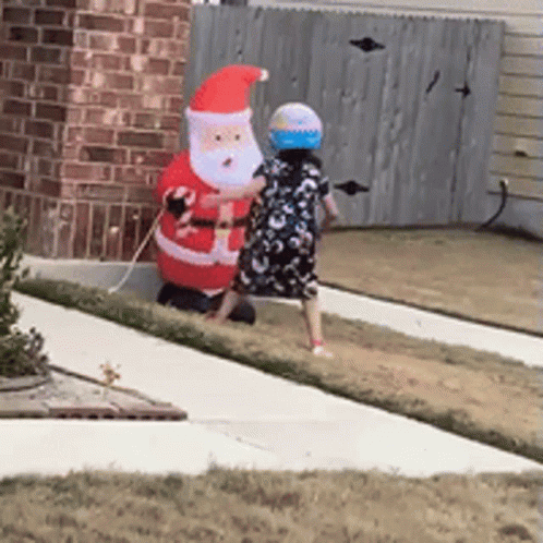 Little Girl Next To Large Inflatable Santa Claus GIF