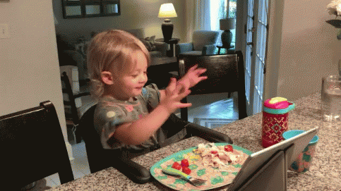 Little Girl Sits at Table With Plate of Food