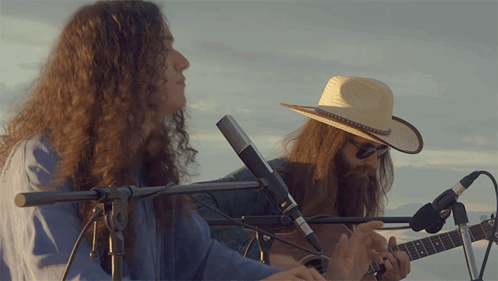 Long Hair Man in Cowboy Hat Playing Guitar With Two Microphones