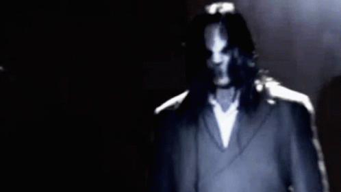 Long-Haired Man In Suit Standing In Dark GIF