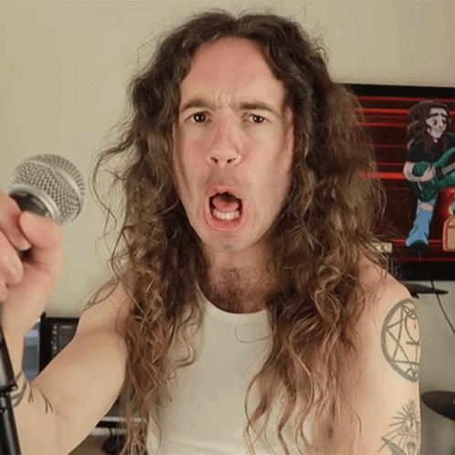 Long Haired Man Singing Into Microphone With Arm Tattoo