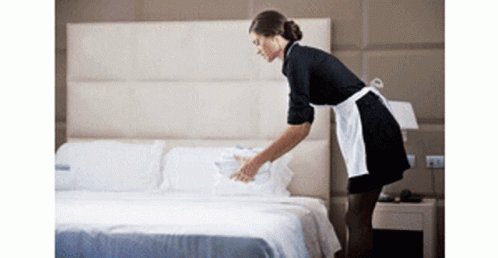 Maid in Apron Making Bed in Hotel Room