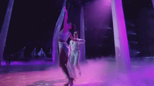 Man and Woman Dancing on Stage With Purple Lights