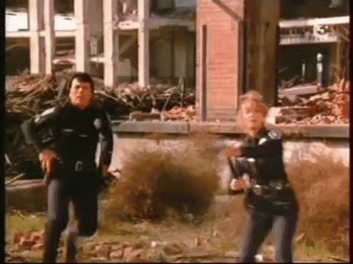 Man and Woman Holding Guns at Destroyed Building